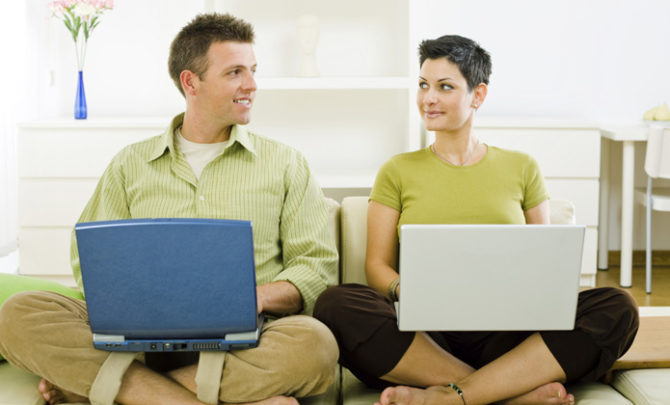 Young couple sitting on sofa, using laptops
